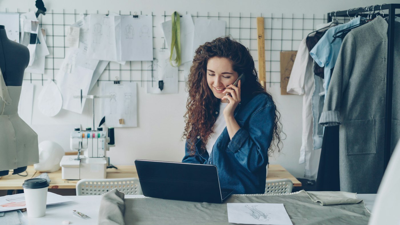 Small business owner on the phone while working on a laptop in her fashion design studio